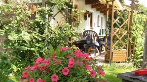 A wooden planter with pink flowers, a wooden pergola, and a dining area with chairs and a table. - Cozy Apartment in Embach Austria near Ski Area (Lend)
