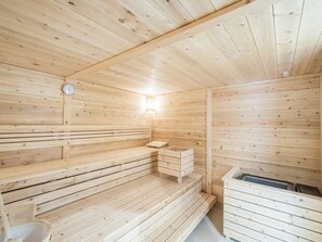 A wooden sauna with benches, a bench with a small table, and a bench with a storage box.