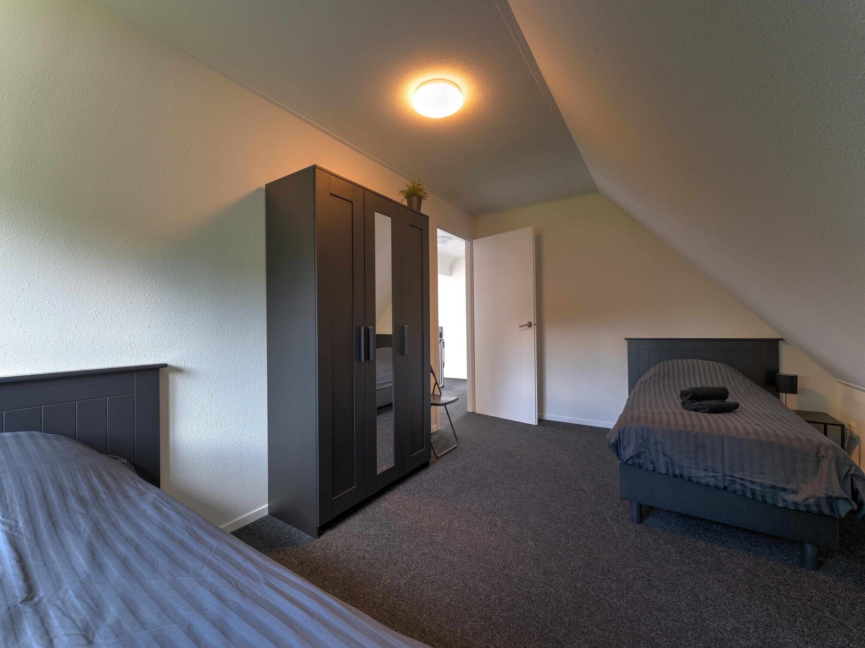 A bedroom with two beds, a wardrobe, a ceiling light, and a door leading to another room.