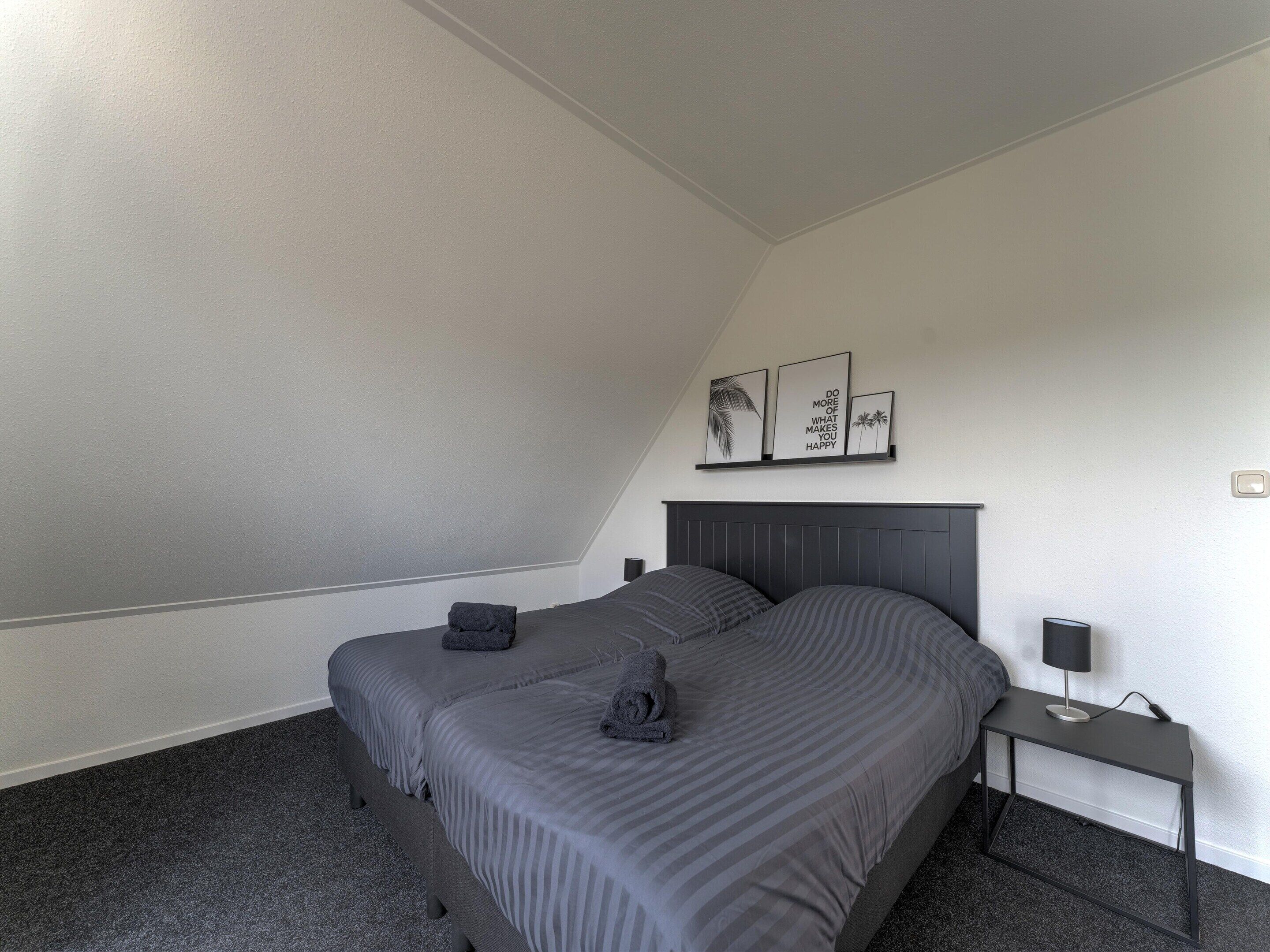 A bedroom with a bed, a nightstand, and a wall-mounted shelf with three framed pictures.