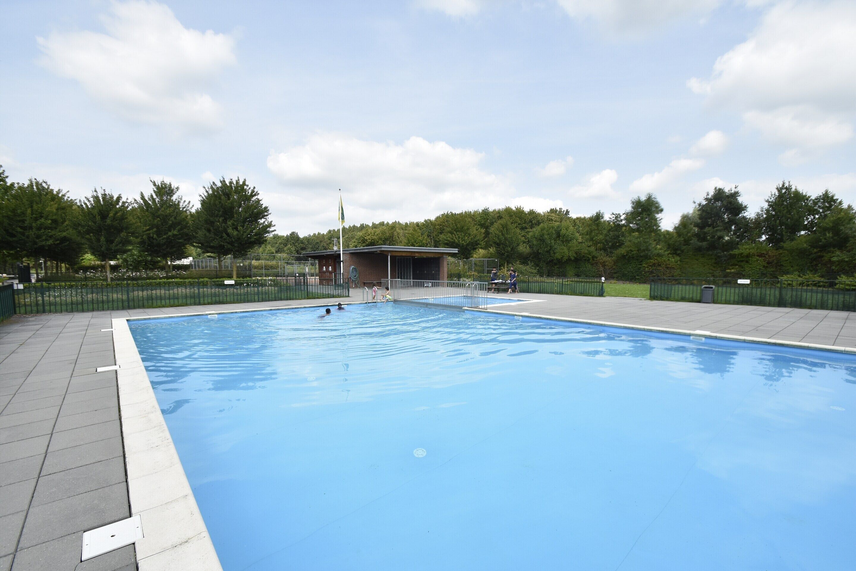 A swimming pool with a tiled deck, a covered seating area, and a flagpole.
