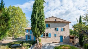 A two-story stone house with blue shutters, a stone pathway, and surrounding greenery. - Villa in Saignon With Pool and Scenic Views (Saignon)