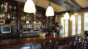 A bar area with wooden bar counter, multiple liquor bottles, glasses, and hanging pendant lights. - Nice Villa in Wieringer Style near Wadden Sea (Hippolytushoef)