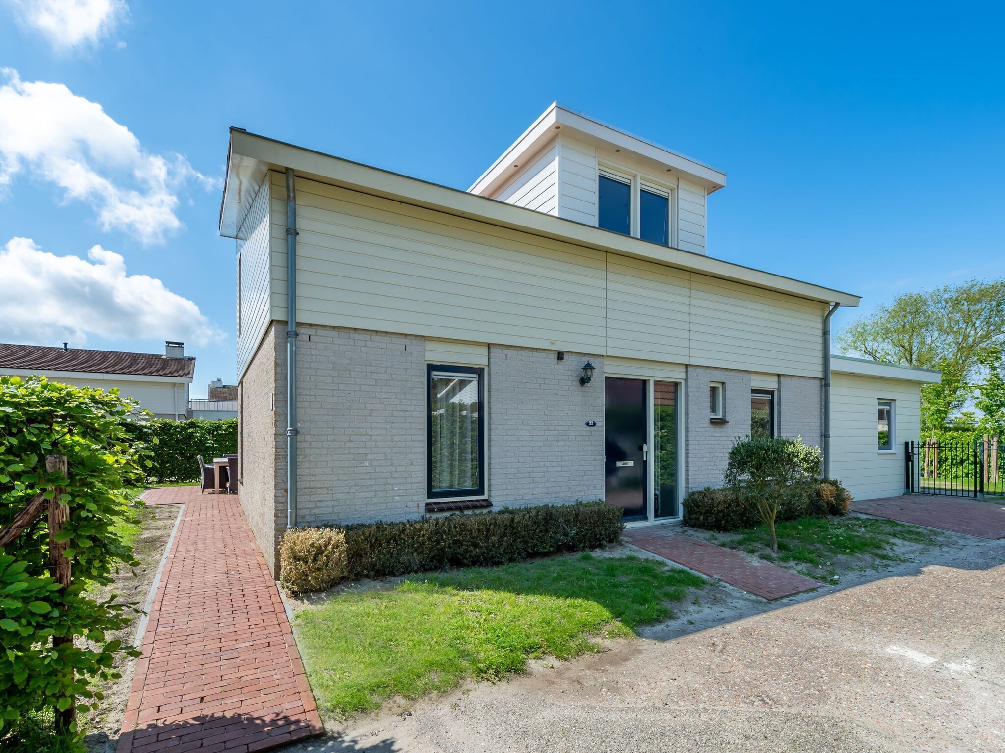 A modern two-story house with a flat roof, a brick pathway, and a small garden area.