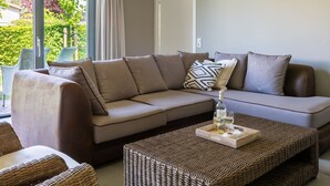 A modern living room with a beige sofa, wicker ottoman, and a tray with glasses and a bottle. - Detached House Zeeland Near Beach (Kamperland)