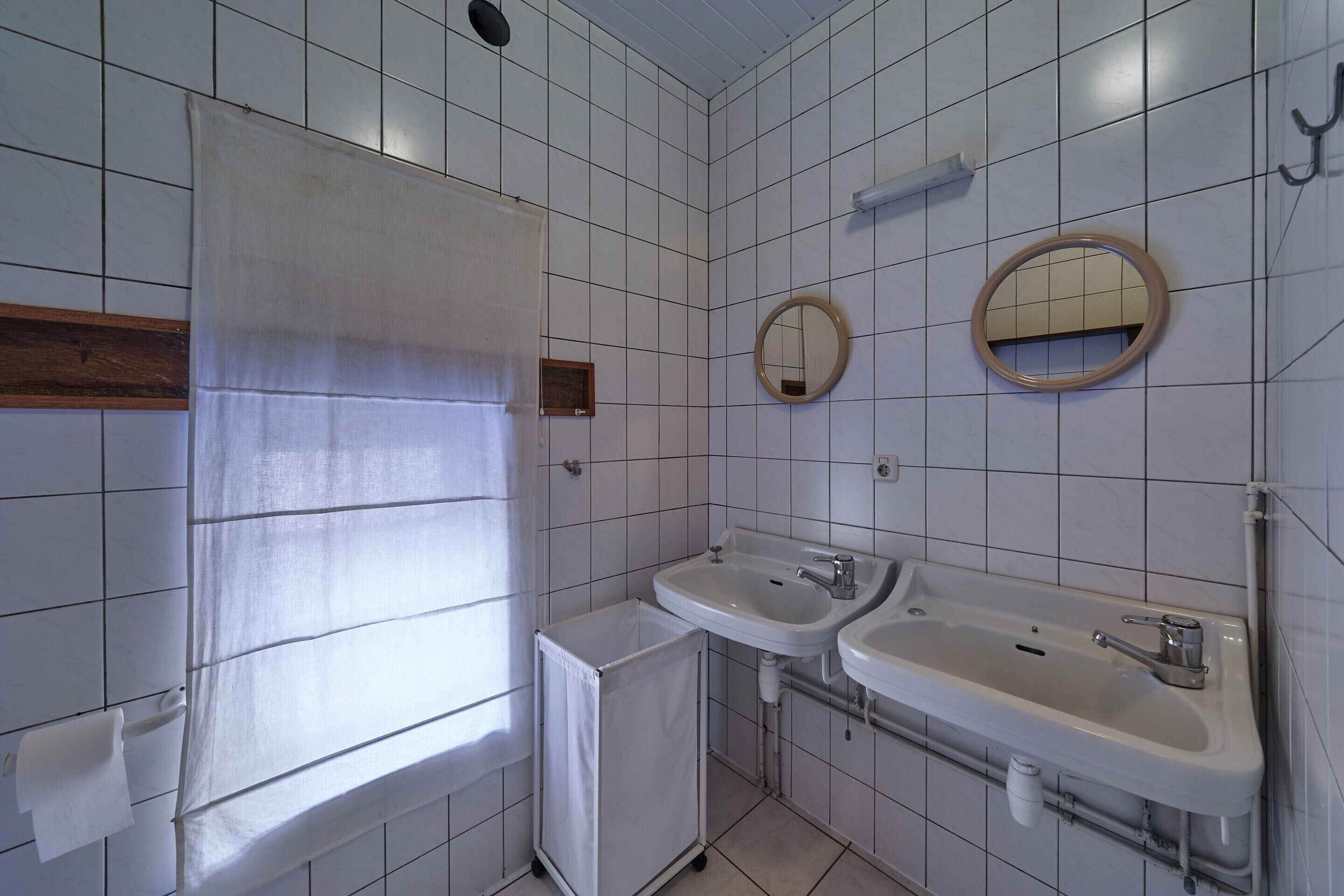 A bathroom with white tiled walls, two sinks, a mirror, and a towel rack.