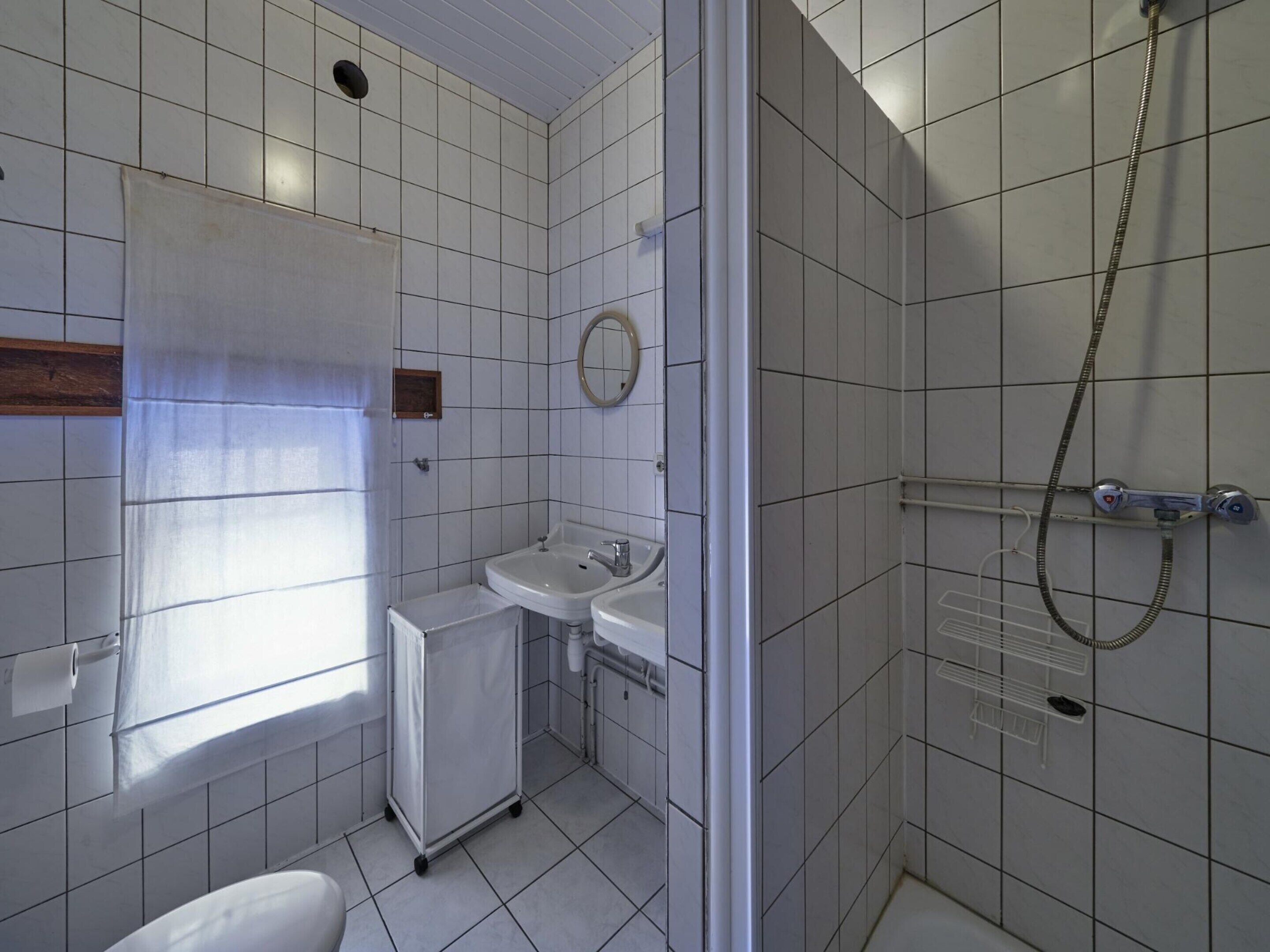 A bathroom with a shower, two sinks, a toilet, and a window.