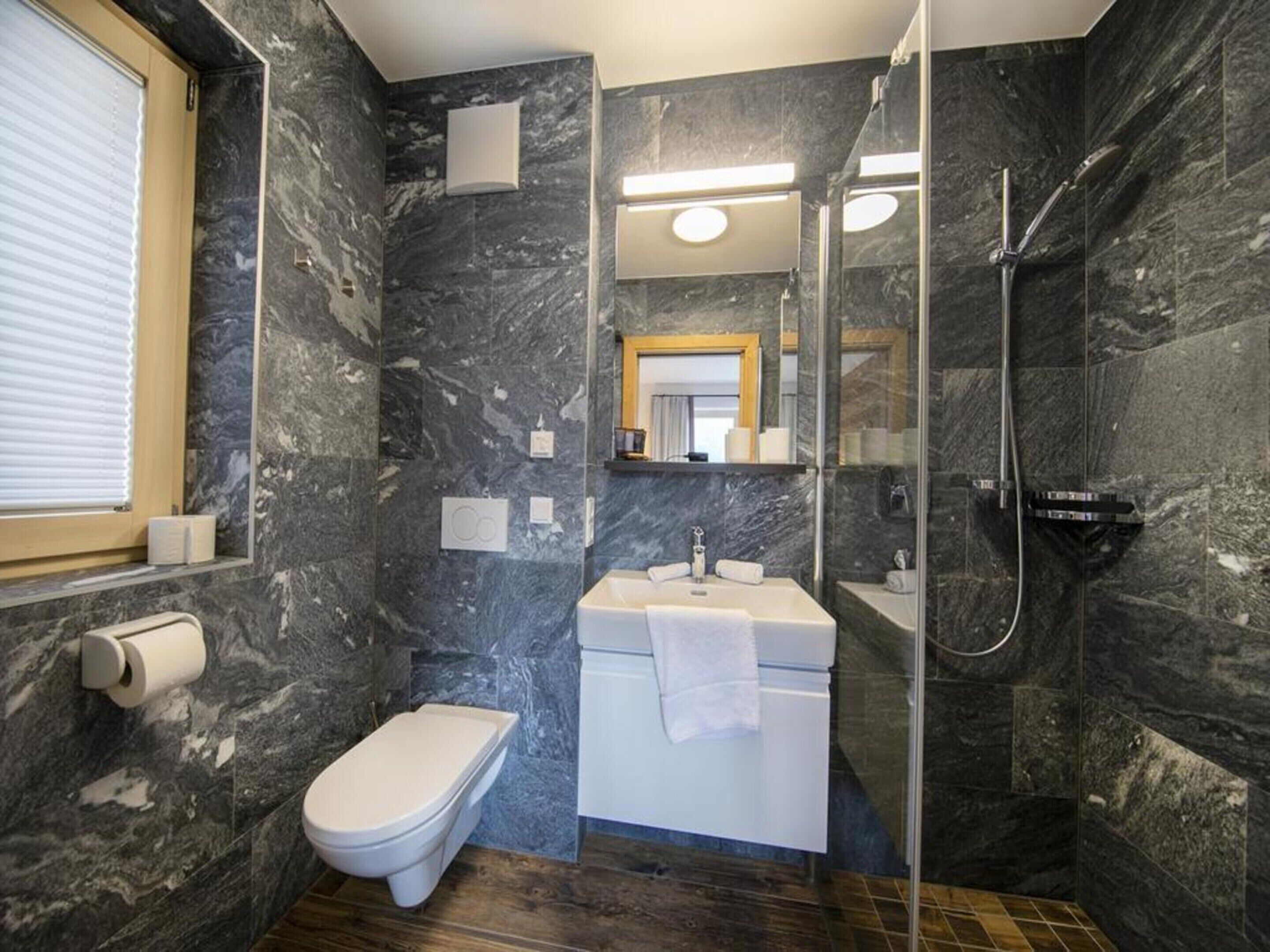 Un baño moderno con pared de mármol, inodoro, lavabo con toalla y zona de ducha.