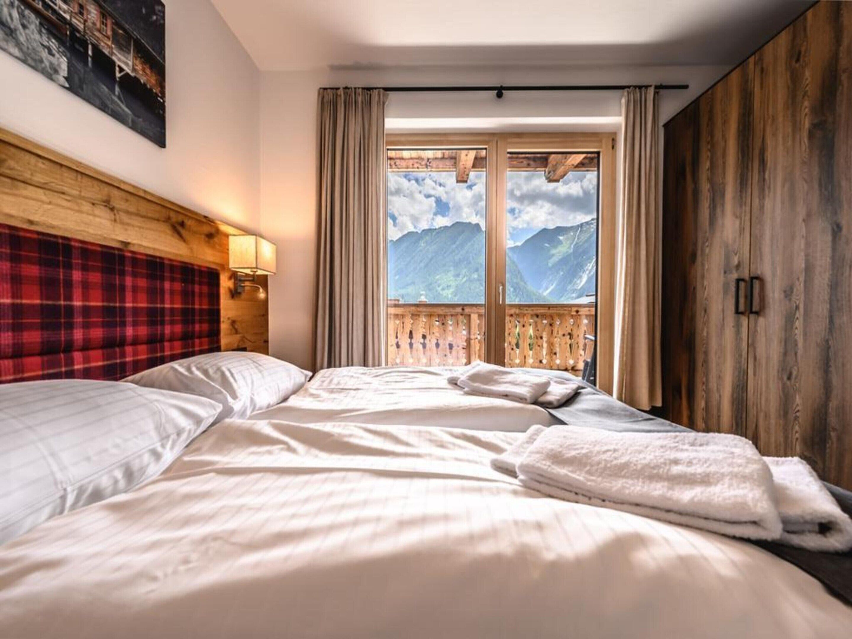 A hotel room with a bed, a wooden headboard, a view of mountains, and a balcony with curtains.