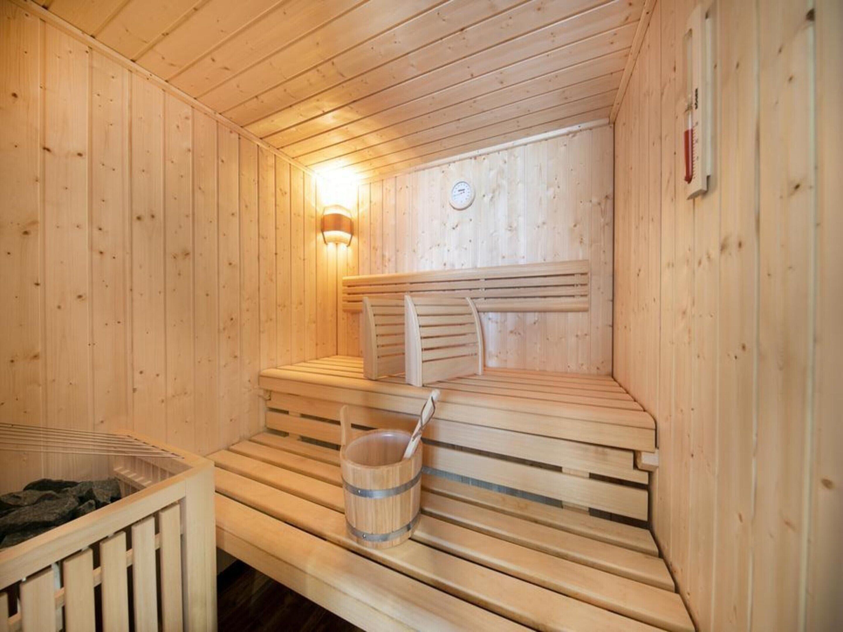 A wooden sauna with benches, a wall-mounted heater, and a wooden bucket with a handle.