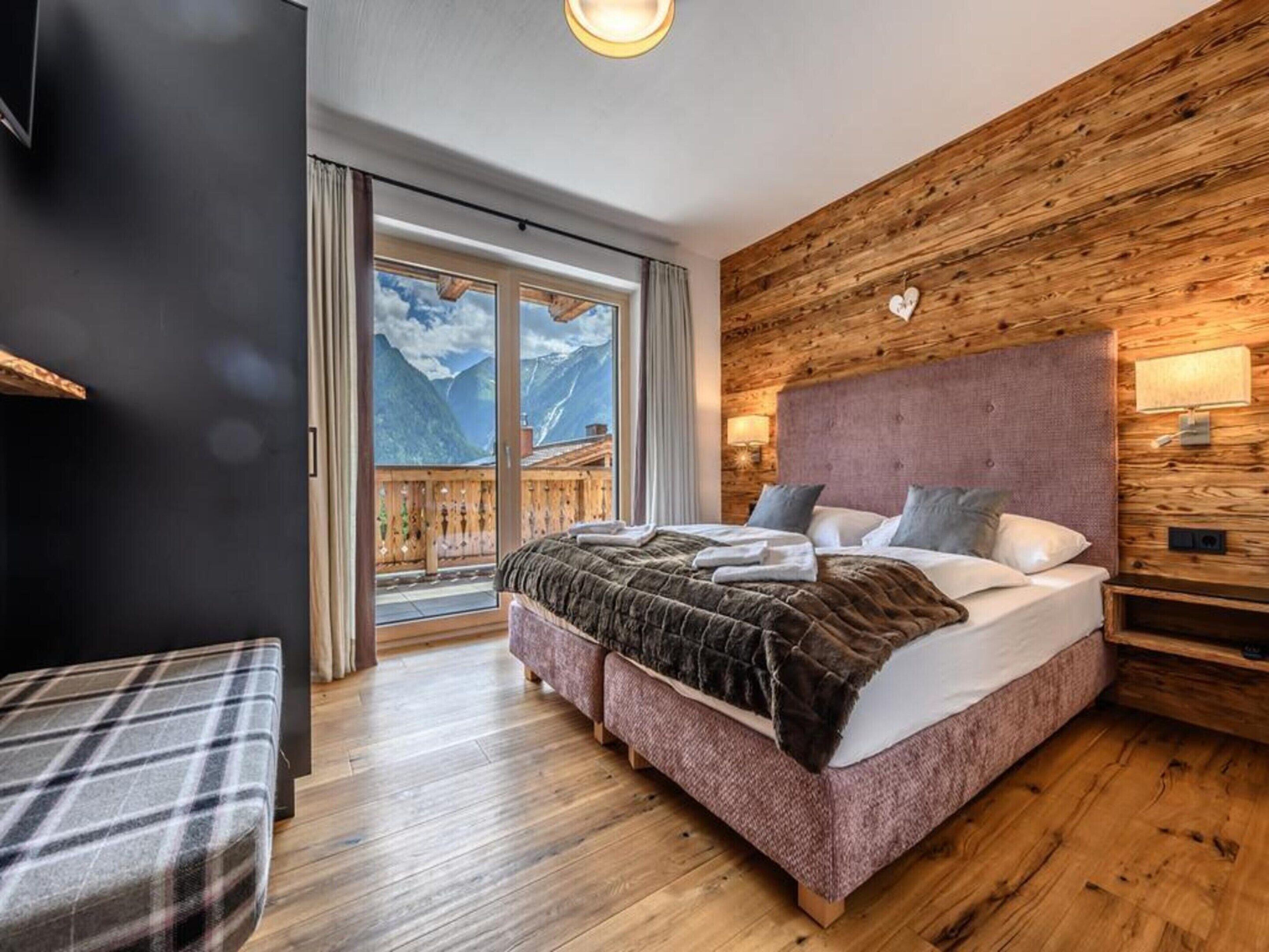 A bedroom with a large bed, wooden walls, a balcony with a mountain view, and a sliding door.
