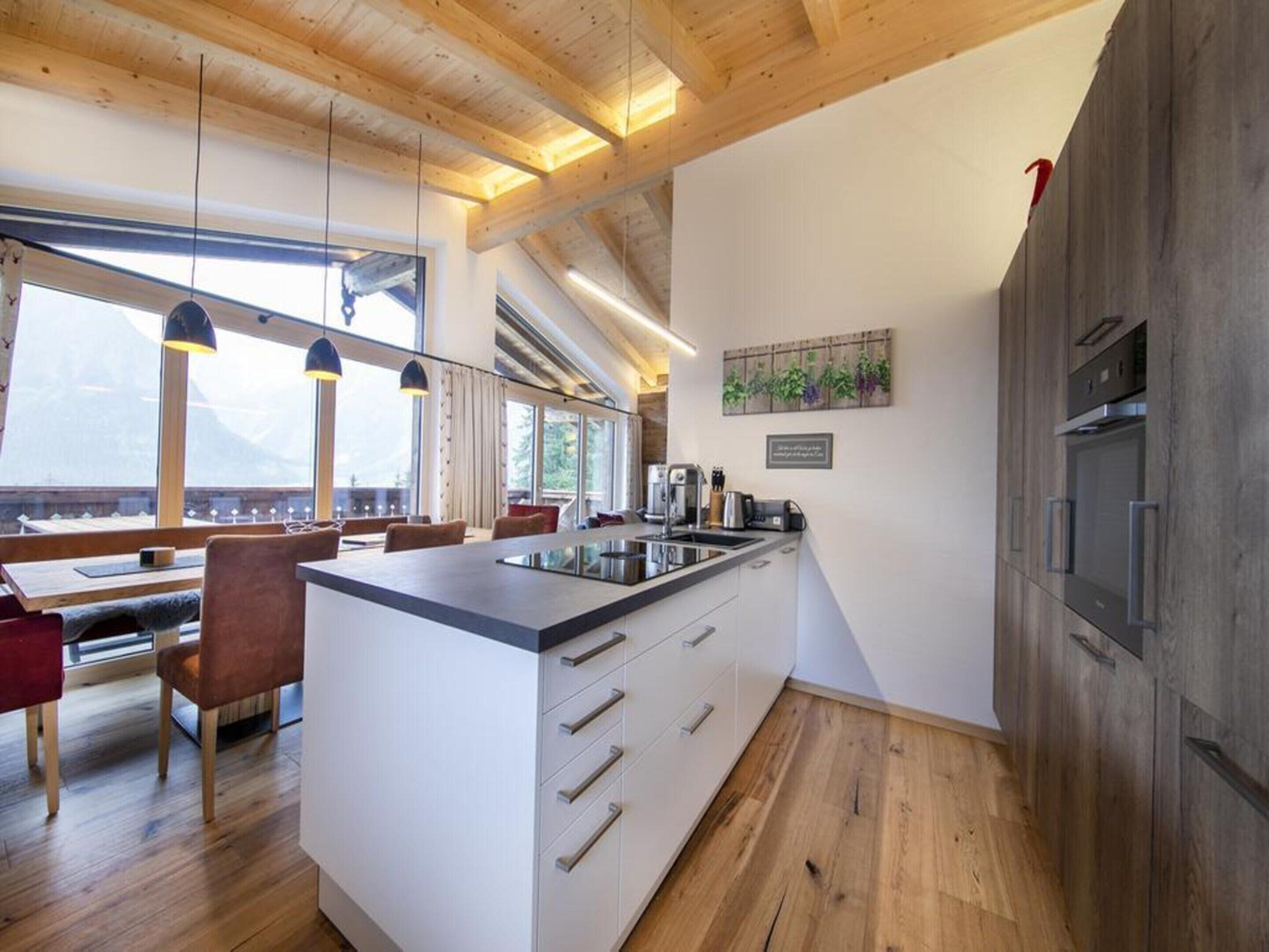 Eine moderne Küche mit einer zentralen Kochinsel, Holzböden und großen Fenstern, die einen Blick ins Freie ermöglichen.