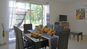 Zona pranzo con tavolo apparecchiato per due, televisore e un quadro appeso al muro.
