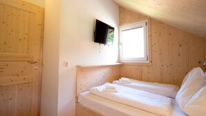 A small, wooden-paneled room with two single beds, a television mounted on the wall, and a window providing natural light. - Attractive Chalet With hot tub (Sankt Georgen am Kreischberg)