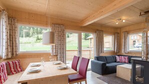 A wooden cabin interior with a dining table set for four, a sofa, and a fireplace. - Attractive Chalet With hot tub (Sankt Georgen am Kreischberg)