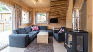 A cozy cabin interior with a sectional sofa, a small wooden table, a glass-fronted cabinet, and a wood-burning stove. - Attractive Chalet With hot tub (Sankt Georgen am Kreischberg)