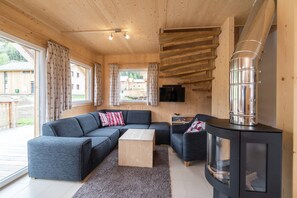 A cozy cabin interior with a sectional sofa, a small wooden table, a glass-fronted cabinet, and a wood-burning stove. - Attractive Chalet With hot tub (Sankt Georgen am Kreischberg)