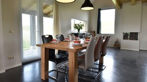 A dining area with a wooden table, black and white chairs, and pendant lighting. - Seaside Villa With Garden (Tzummarum)