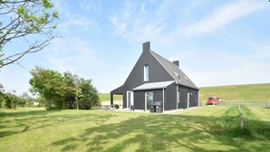 A modern black barn with a sloped roof, a picnic table, and two trash bins in front. - Seaside Villa With Garden (Tzummarum)