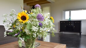 A living room with a wooden coffee table holding a vase of flowers. There is a black cabinet and a window in the background. - Seaside Villa With Garden (Tzummarum)