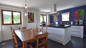A modern kitchen with a dining area, featuring a large island, wooden chairs, and colorful artwork on the walls. - Luxe Villa in Montbrun (Montbrun-des-Corbières)
