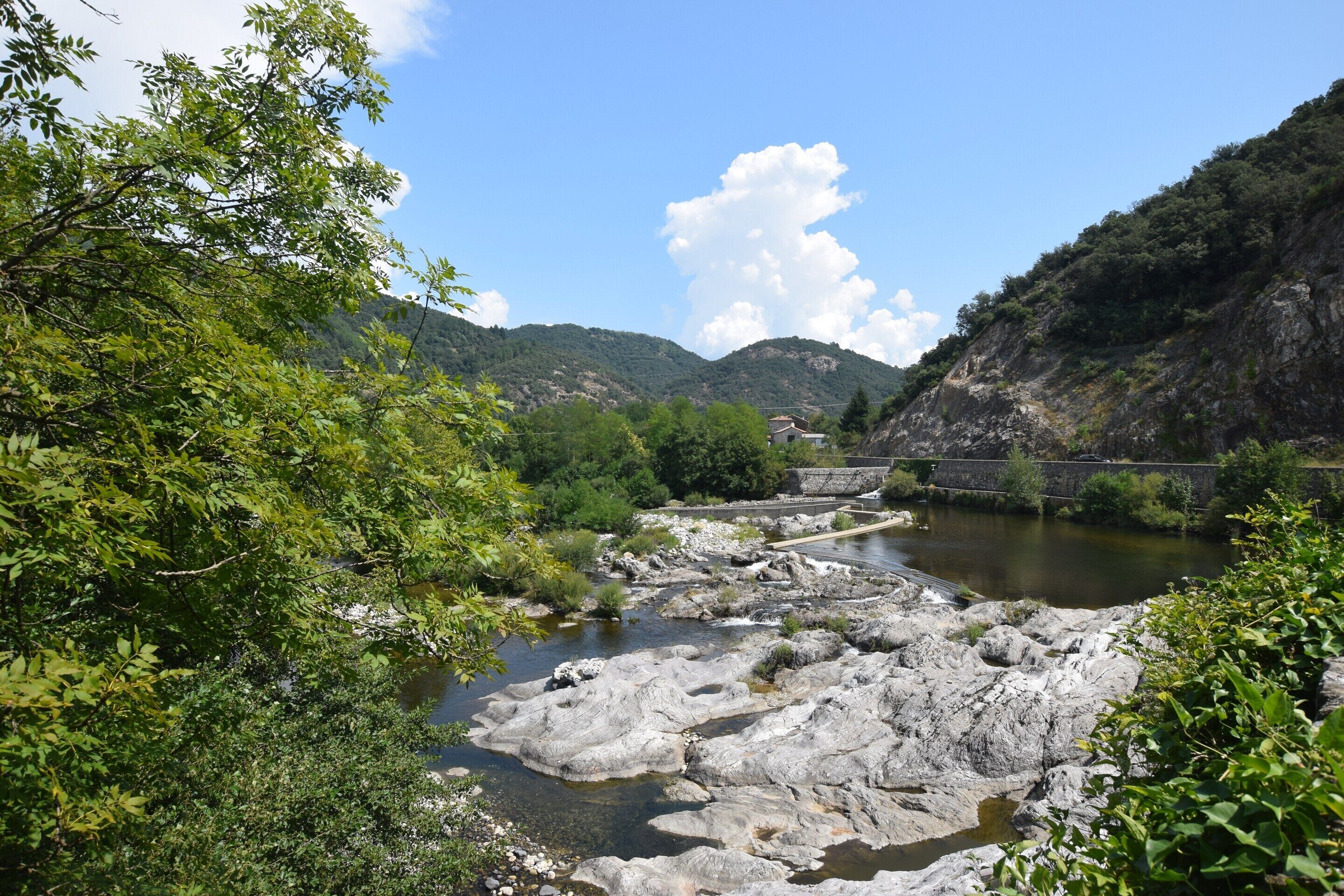 A river with rocky terrain, a bridge, and a mountainous backdrop.