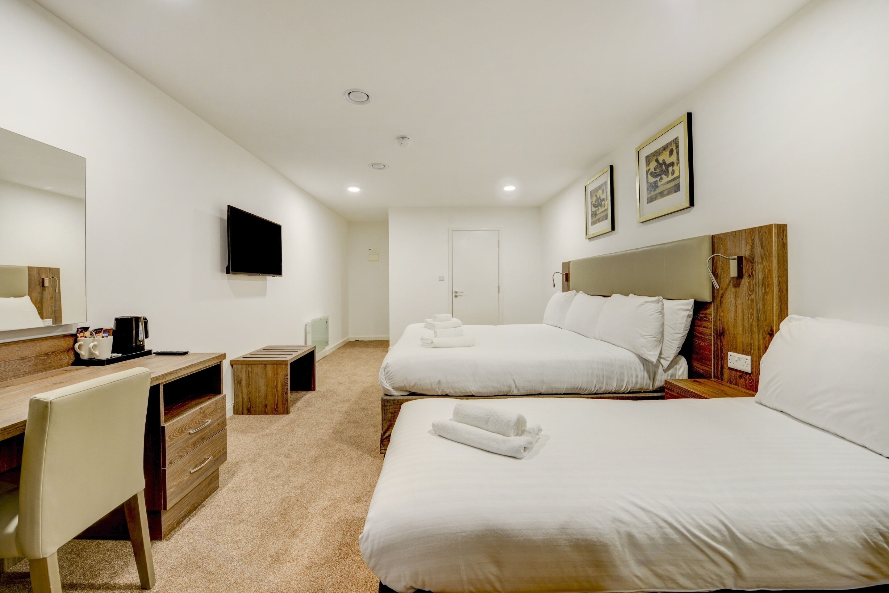 A hotel room with two beds, a desk, a chair, a flat-screen TV, and a door.