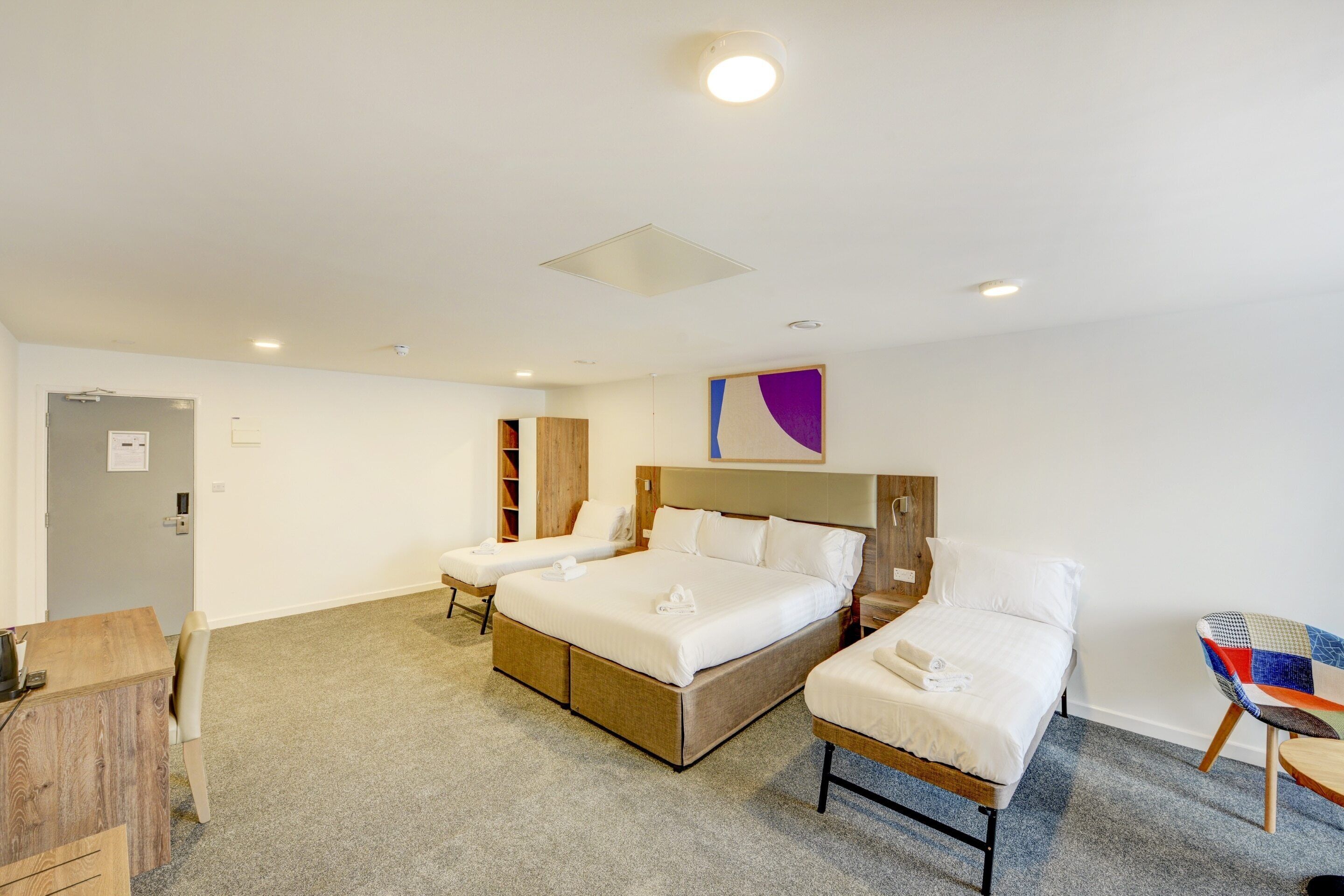 Une chambre d’hôtel avec un grand lit, un lit plus petit, un bureau et une chaise.