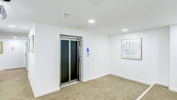 A clean, modern hallway with a carpeted floor, a door with a glass panel, and a framed artwork on the wall.
