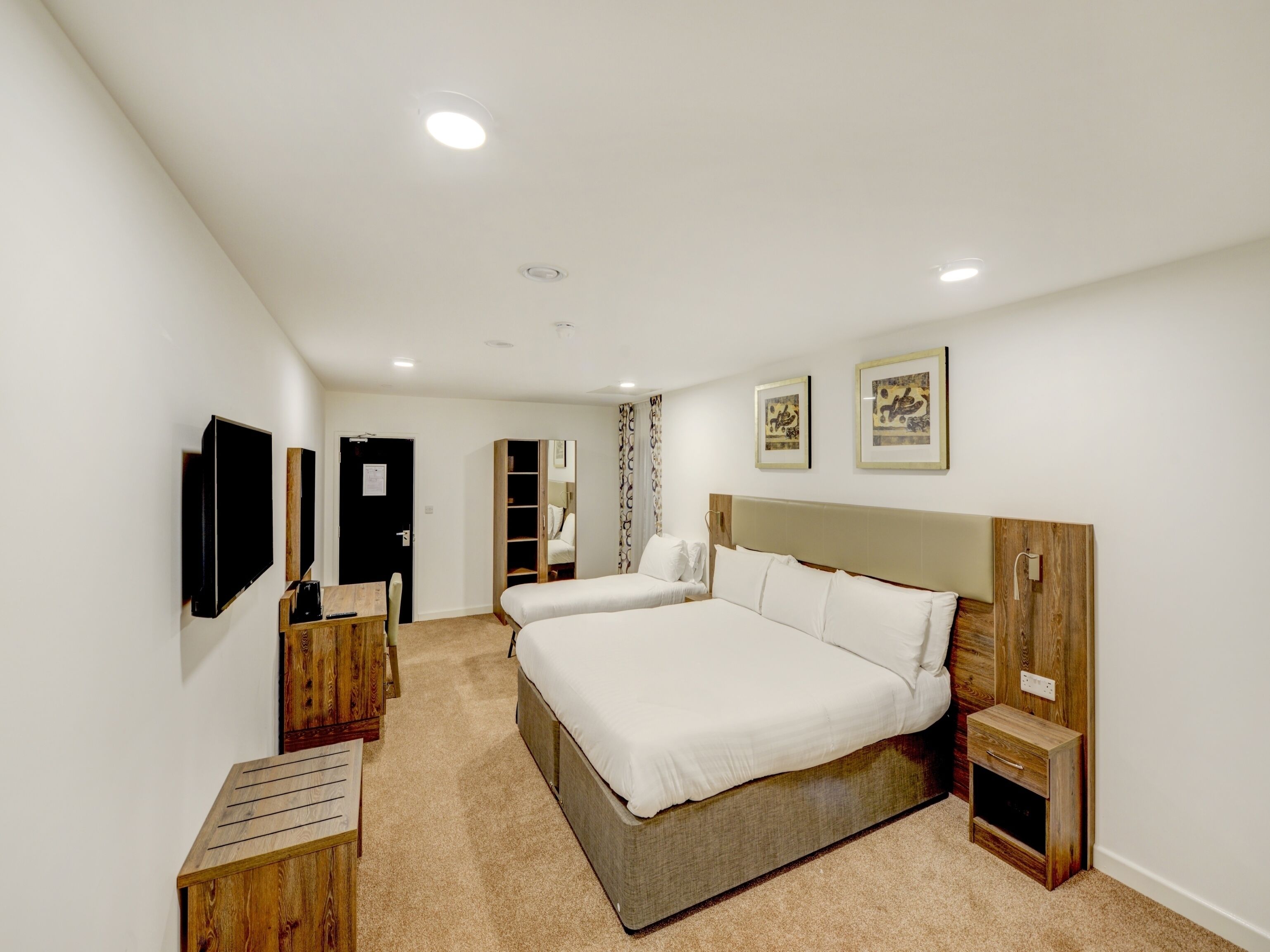 A modern bedroom with two beds, a TV, a wooden desk, and a wardrobe.