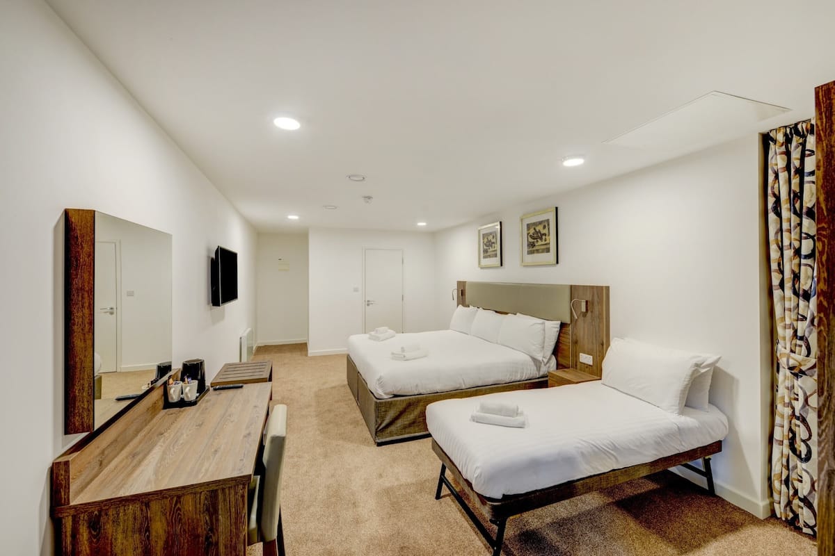 Une chambre d’hôtel avec deux lits, un bureau en bois, un téléviseur à écran plat et un grand miroir.