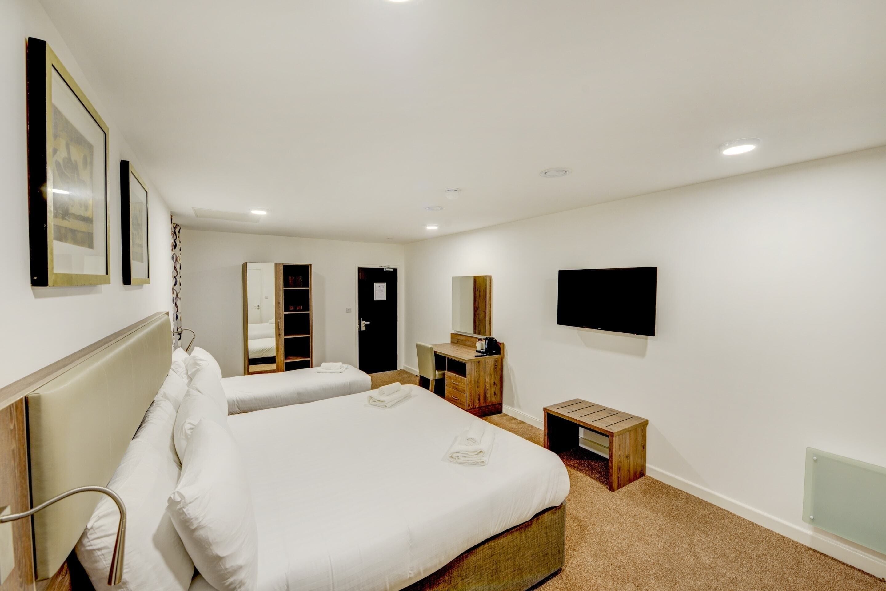 A hotel room with two beds, a desk, a mirror, a TV, and a wardrobe.