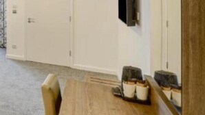 Una habitación de hotel con una mesa de comedor de madera, un televisor montado en la pared y un espejo grande.