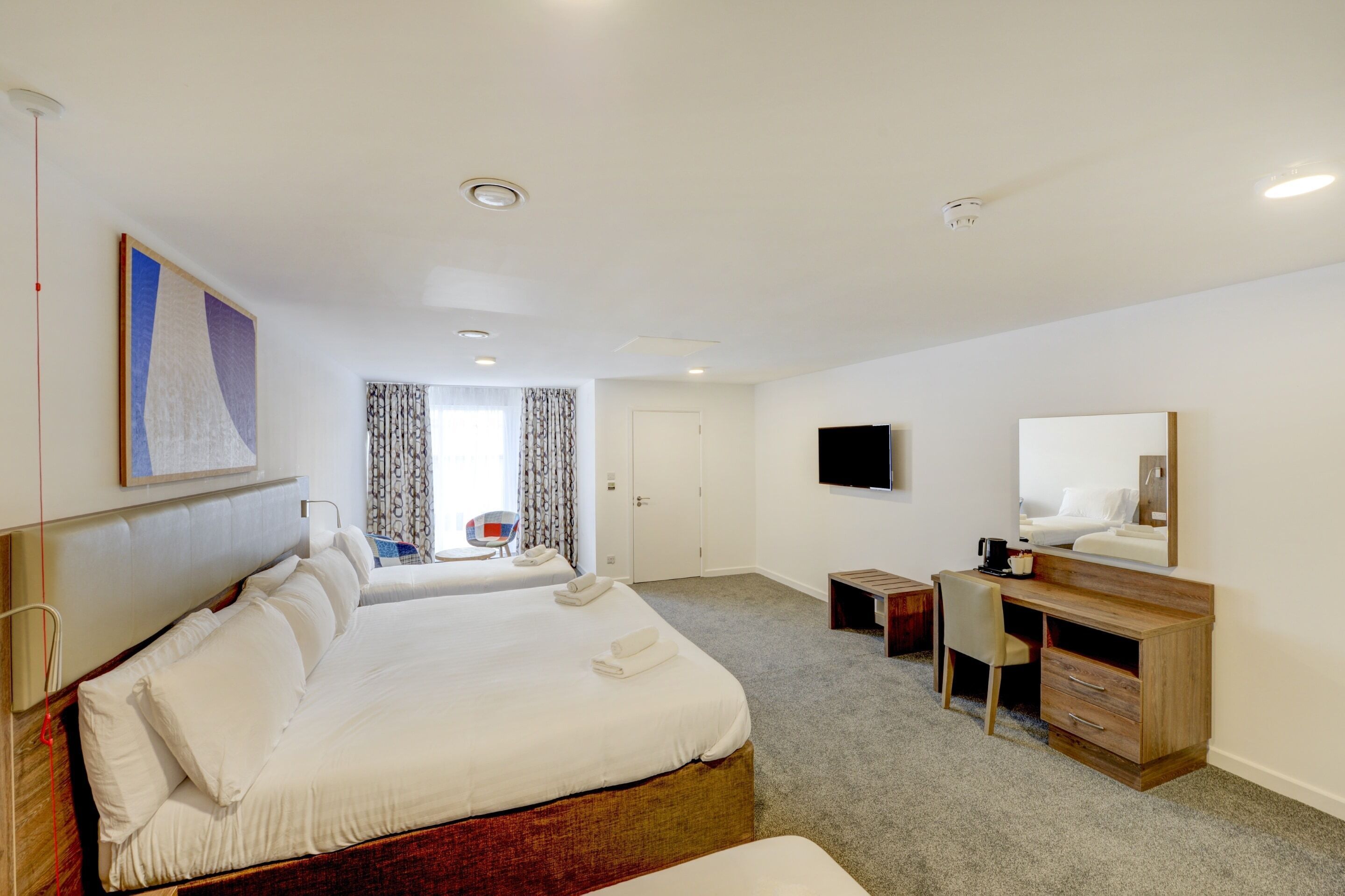 Habitación de hotel con una cama grande, un escritorio, una silla, un televisor y un baño visible a través de una puerta.