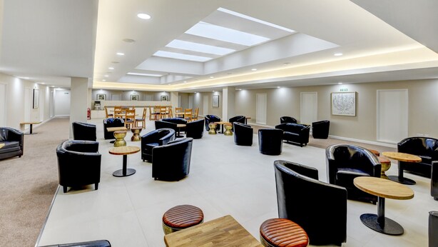 Amplia sala de estar con diversas opciones de asientos, incluyendo sofás y sillones, distribuidos alrededor de mesas.