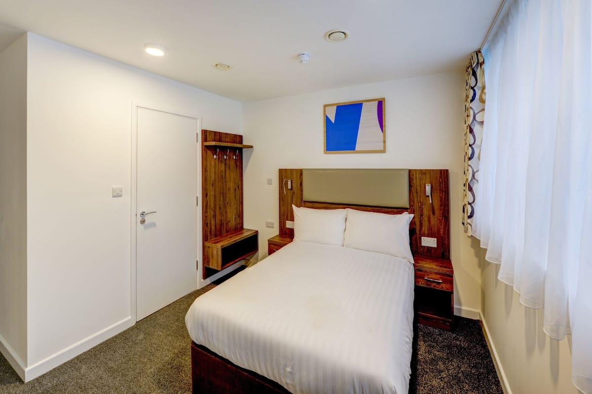 Une chambre d’hôtel comprenant un lit, une armoire en bois, une table de chevet et une œuvre d’art accrochée au mur.