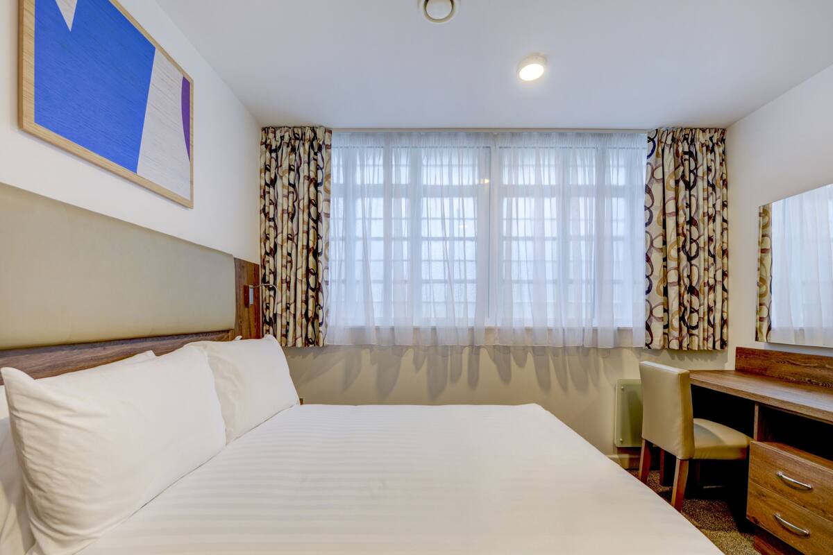 Une chambre d’hôtel avec un grand lit, un bureau, une chaise et un miroir.