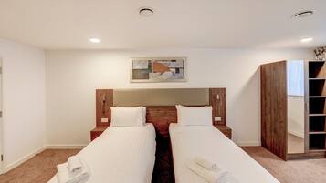 A hotel room with two single beds, a wooden headboard, a large mirror, and a framed abstract artwork on the wall.