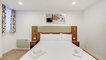 Habitación de hotel con una cama grande, cabecera de madera, dos mesitas de noche, un calentador verde y una ventana con cortinas estampadas.