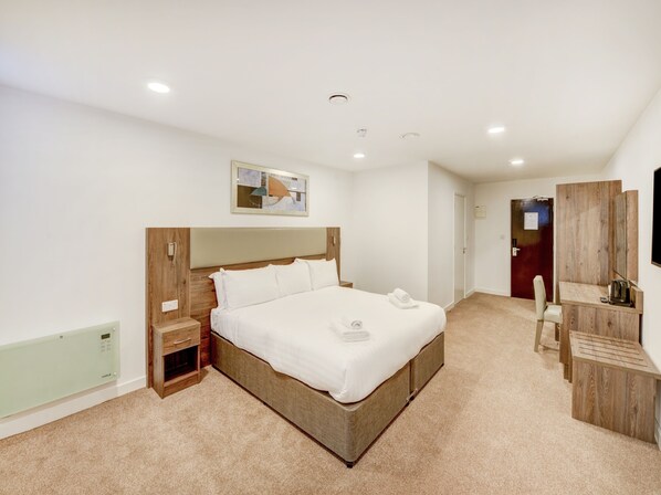 A modern hotel room with a large bed, a wooden headboard, a bedside table, a desk with a chair, and a flat-screen TV. - OYO Plymouth Central Hotel (Plymouth)
