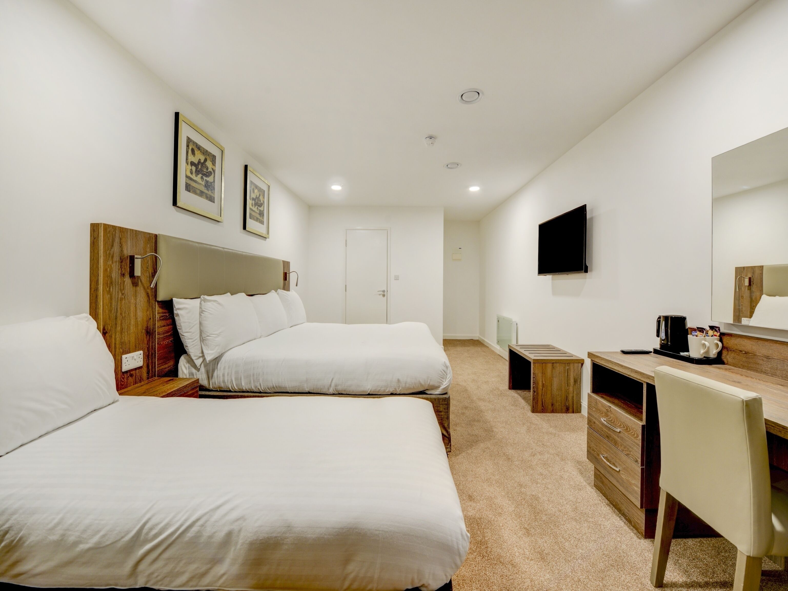 Quarto de hotel com duas camas, uma escrivaninha, uma cadeira, uma televisão e uma cafeteira.