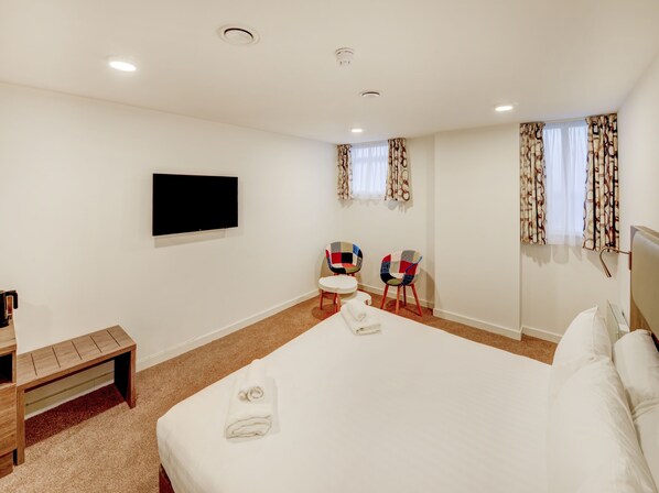 A hotel room with a large bed, a flat-screen TV mounted on the wall, two colorful chairs, a small table, and a bench. - OYO Plymouth Central Hotel (Plymouth)