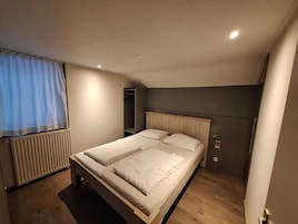 A small, well-lit bedroom with a single bed, a radiator, a wardrobe, and a window with curtains.
