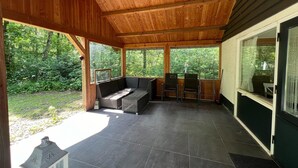 A covered patio area with a seating arrangement, a small table, and a view of the surrounding greenery. - Holiday Home in Stramproy Near Nature Reserve (Stramproy)