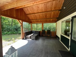 Un patio cubierto con una zona de estar, una mesita y vistas a la vegetación circundante.