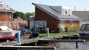 A marina with docked boats, a wooden building with a sloped roof, and a red car parked nearby. - House by Uitgeestermeer With Garden (Uitgeest)
