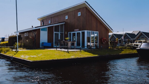 A wooden building with a large glass door, a small garden, and a canal in front. - House by Uitgeestermeer With Garden (Uitgeest)