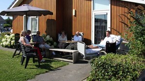 An outdoor seating area with tables and chairs, a wooden building with a large window, and a clear sky. - House by Uitgeestermeer With Garden (Uitgeest)