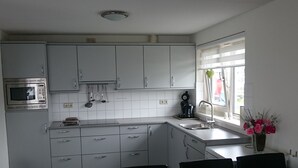 A modern kitchen with white cabinets, a microwave, and a coffee maker. There is a window with a view of the outside, and a vase with flowers on the counter. - House by Uitgeestermeer With Garden (Uitgeest)