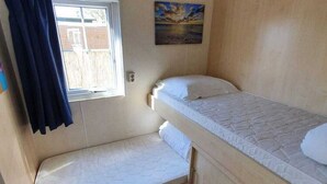 Un petit logement composé d’une seule pièce, avec un lit superposé et une fenêtre avec des rideaux.